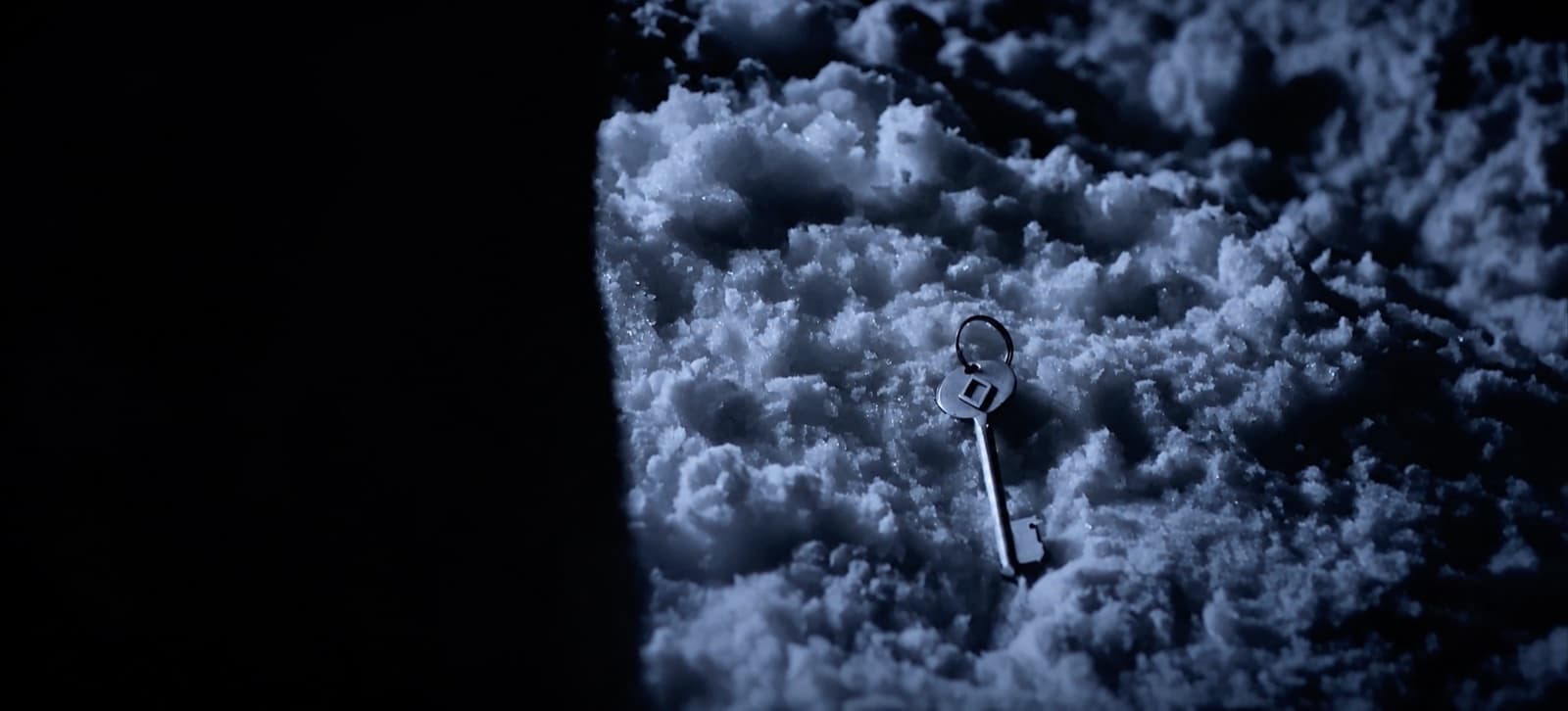 Uma chave de metal caída sobre a neve, à noite, isolada num facho de luz fria