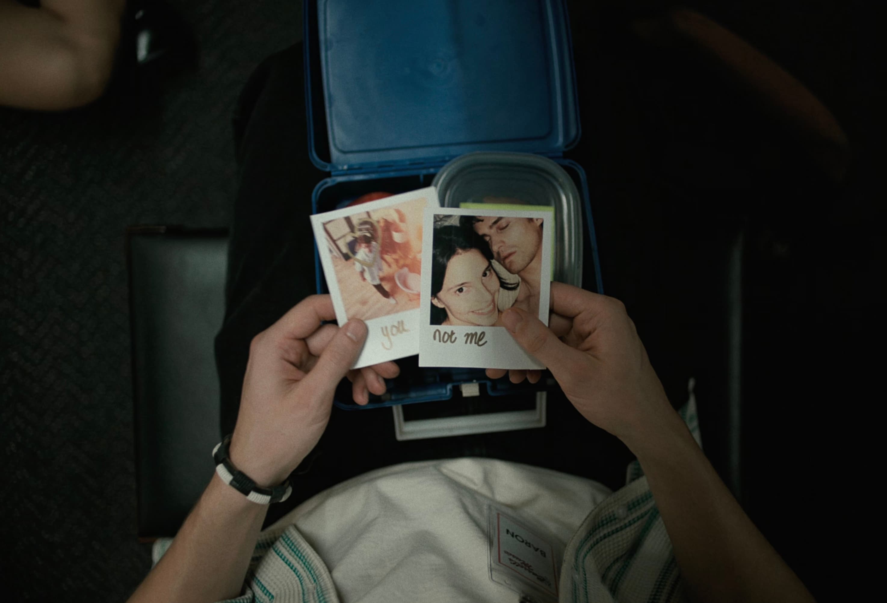 Mãos segurando duas polaroides sobre uma lancheira aberta, uma escrita 'you', a outra 'not me'