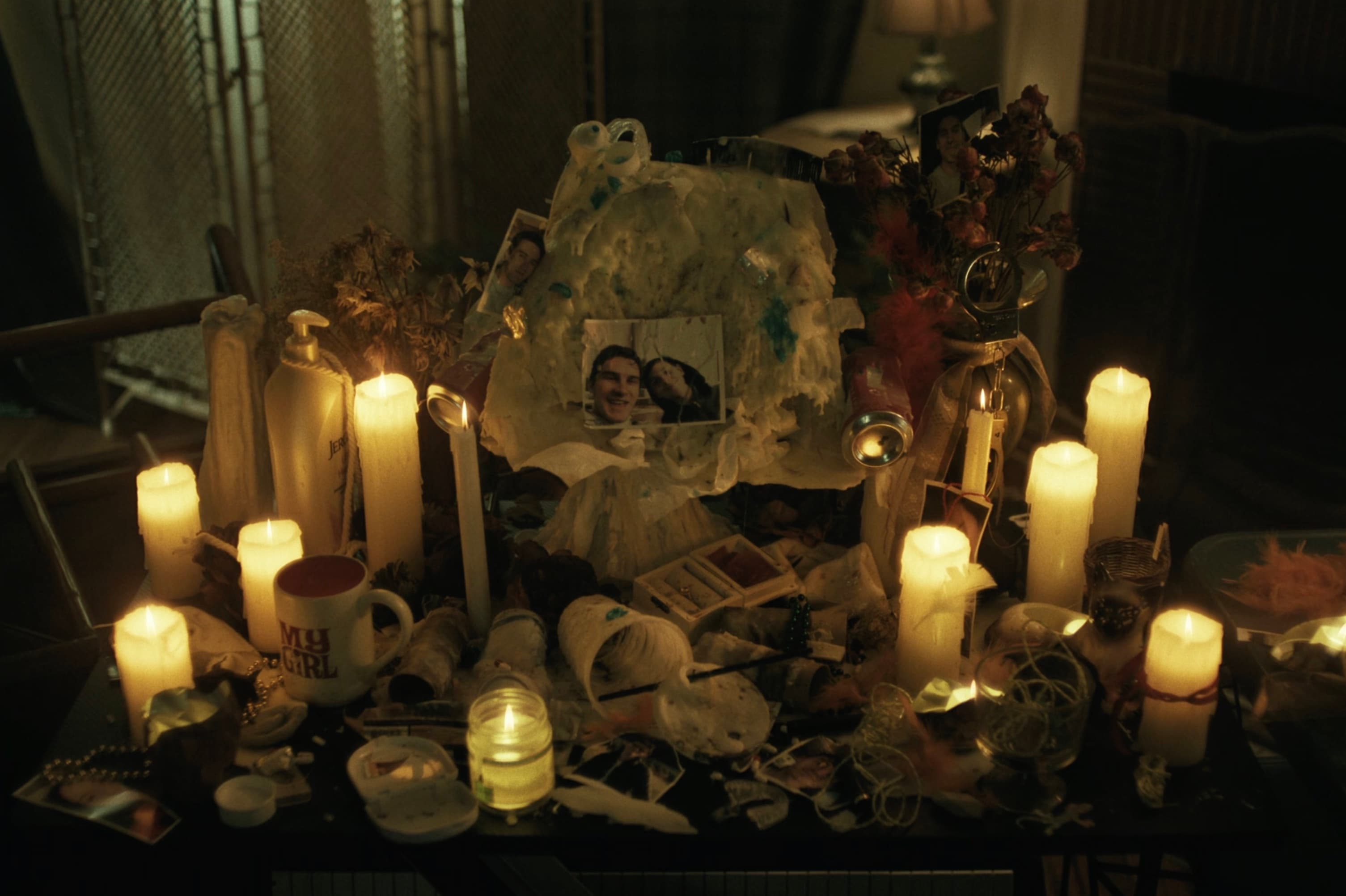 Altar improvisado à luz de velas, coberto de fotos, flores secas e uma caneca escrita 'My Girl'