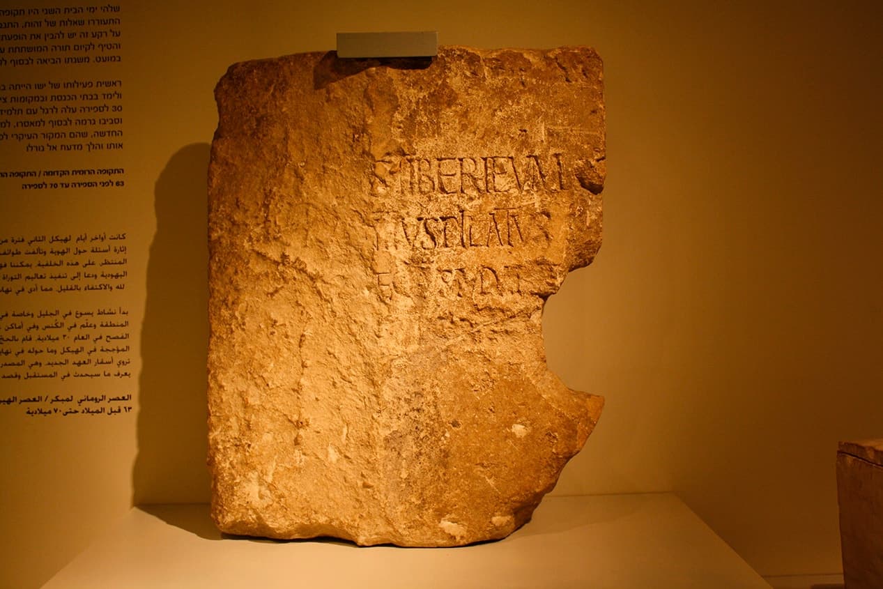 Bloco de calcário antigo e desgastado exposto em um museu, com uma inscrição latina parcialmente preservada onde se leem as palavras TIBERIEVM e PILATVS, conhecido como a Pedra de Pilatos
