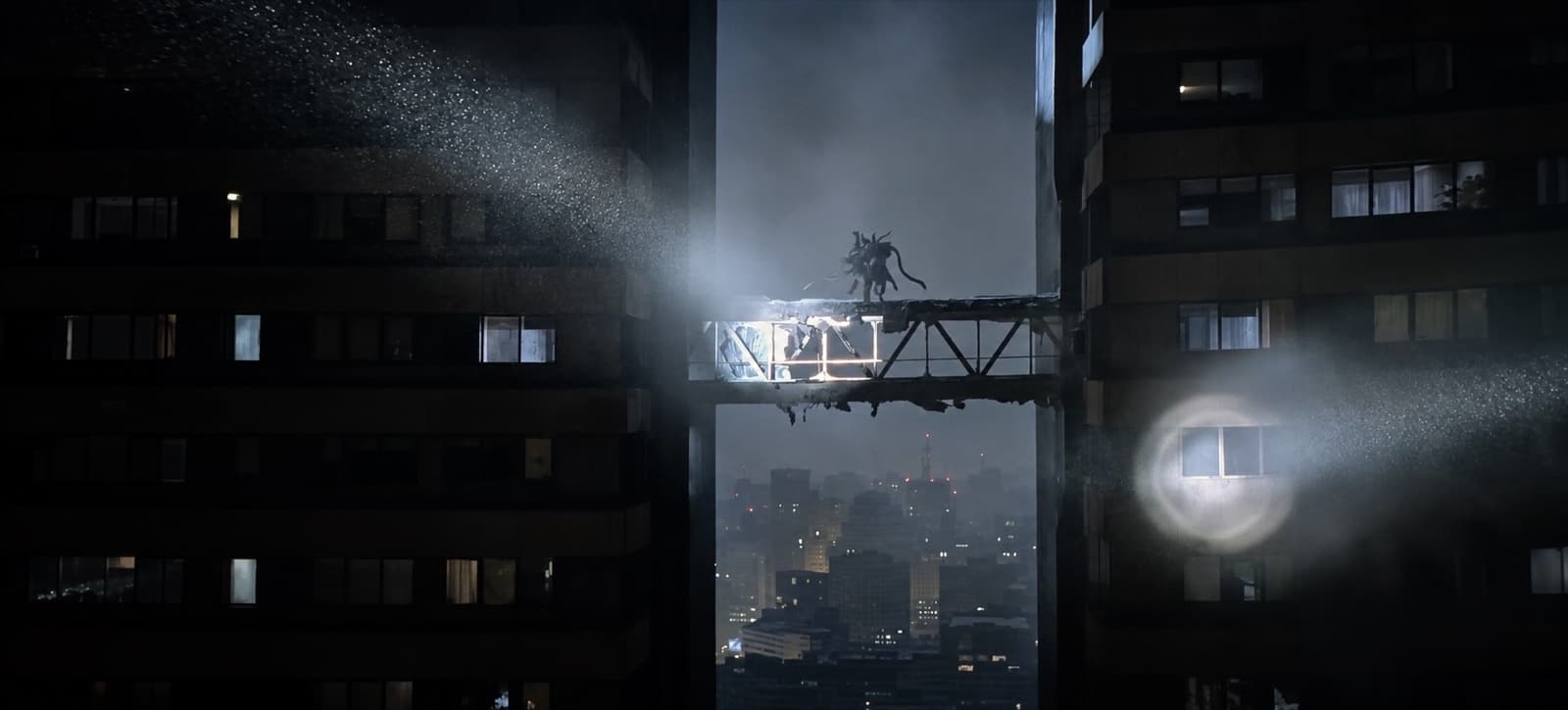 Silhueta de uma criatura sobre uma passarela danificada entre duas torres, à noite, cortada por feixes de holofote, com a cidade na névoa lá embaixo